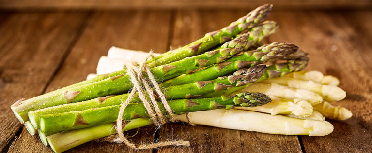 Grüner und weißer Spargel, zusammengebunden mit Jute, auf rustikalem Holzuntergrund präsentiert.