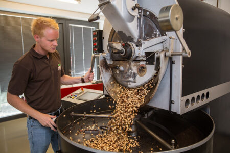 Ein Kaffeeröster entleert frisch geröstete Kaffeebohnen aus einer Maschine in einen großen Behälter.