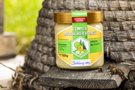 Echter deutscher Honig in einem 500g Glas, präsentiert vor einem Hintergrund aus einem traditionellen Bienenkorb.