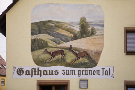 Wandmalerei eines Gasthauses mit Rehen und ländlicher Landschaft, betitelt "Gasthaus zum grünen Tal".