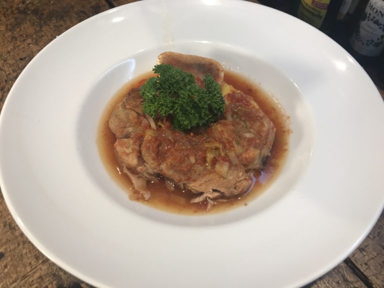 Ossobuco vom Kalb in Tomatensauce, garniert mit frischer Petersilie, serviert auf Parmesan-Polenta.