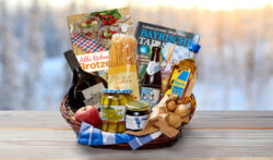 Ein Geschenkkorb mit bayerischen Delikatessen, Kochbuch, Getränken und regionalen Produkten auf einem Holzuntergrund.