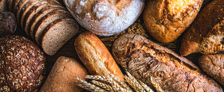 Eine Auswahl verschiedener Brotsorten, darunter Vollkorn, Baguette und Brötchen, auf einem Holztisch.
