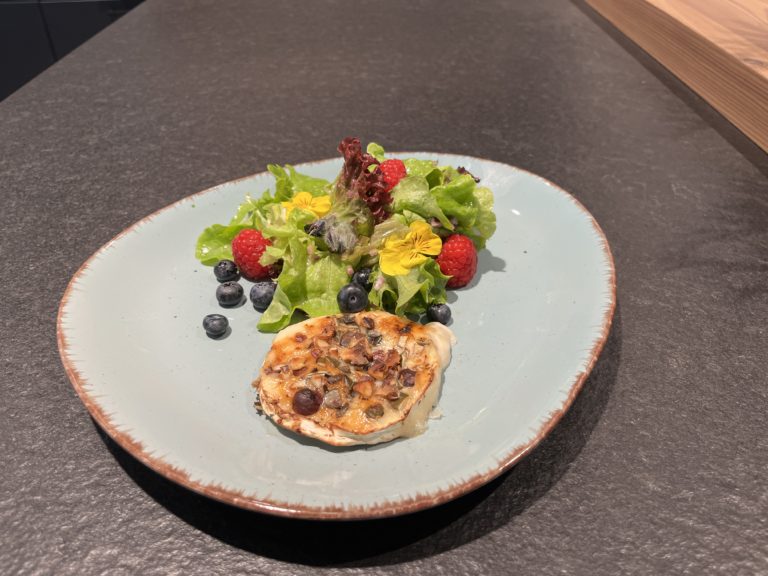 Warmer Ziegencamembert mit buntem saisonalem Salat, Himbeeren und Heidelbeeren auf einem flachen Teller.