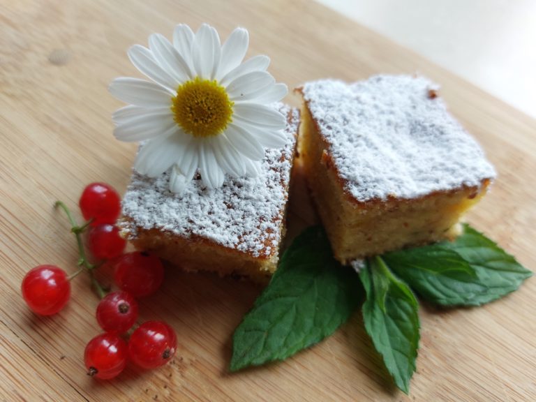 Zucchinikuchen mit Puderzucker, frischen roten Johannisbeeren und einer Blume auf einem Holzbrett dekoriert.