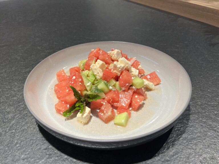 Frischer Salat aus Wassermelone, Gurke und Feta, garniert mit Minze, serviert auf einem flachen Teller.