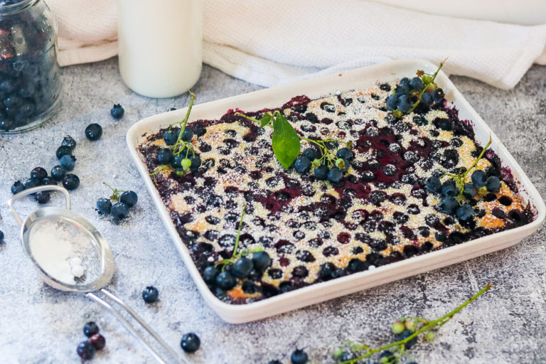Ein köstlicher Heidelbeerauflauf mit frischen Beeren und Puderzucker, serviert auf einem grauen Tisch.