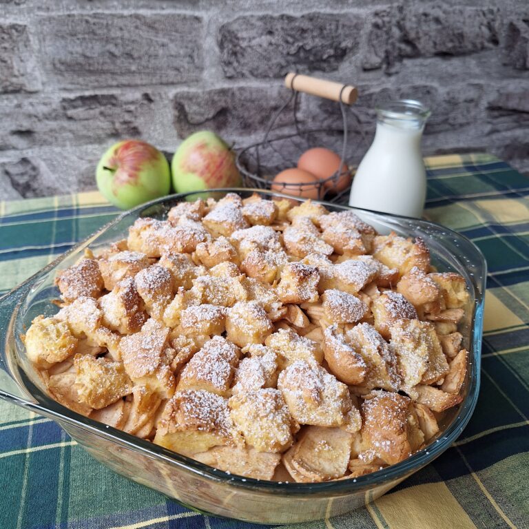Scheiterhaufen mit Vanillesoße, serviert mit Äpfeln, Eiern und Milch auf einem karierten Tisch.