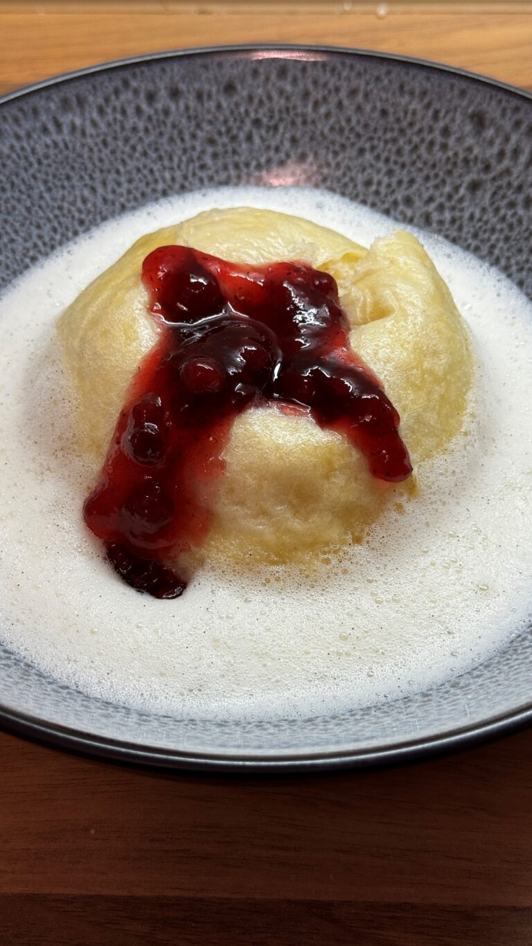Dampfnudeln mit Vanillesoße, bedeckt mit roter Fruchtsoße, serviert in einer dekorativen Schüssel.