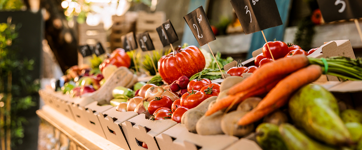 Bunte Auswahl an frischem Gemüse und Obst auf einem Bauernmarkt mit Preisschildern für die Produkte.