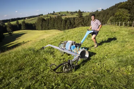 Bauer mit großer Mähmaschine mäht Gras auf Almwiese