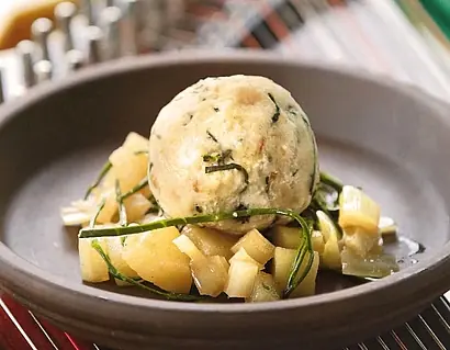 Gourmet-Kasknödel serviert auf einer Schale mit geschmortem Gemüse und frischen Kräutern.