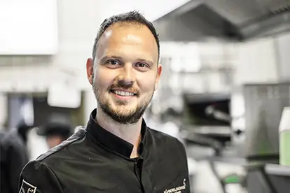 Ein lächelnder Koch in einer modernen Küche, der Professionalität und Leidenschaft für das Kochen ausstrahlt.