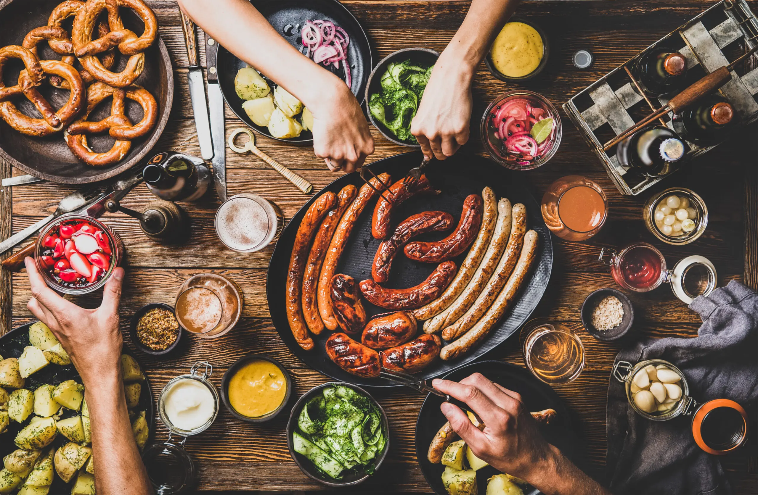 Ein rustikaler Tisch mit verschiedenen Würsten, Brezeln, Beilagen und Getränken, ideal für ein geselliges Essen.