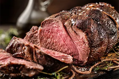 Saftiges, perfekt gegartes Rinderfilet mit rosa Kern, angerichtet auf einem Holzbrett mit frischen Kräutern.
