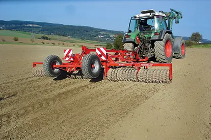 Ein Traktor mit Walze bearbeitet einen Acker, um den Boden zu ebnen und für die Aussaat vorzubereiten.