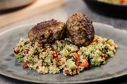 Saftige Frikadellen auf einem Bett aus buntem Couscous-Salat mit Gemüse und Kräutern serviert.