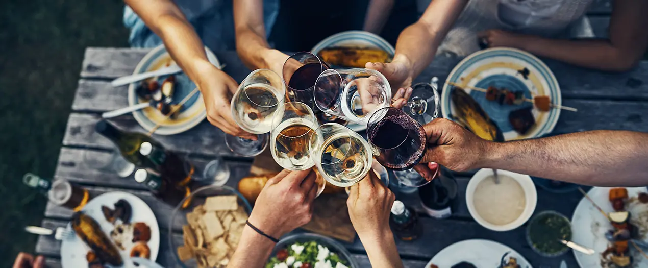 Freunde stoßen mit Weingläsern an, umgeben von köstlichen Speisen auf einem Tisch im Freien.