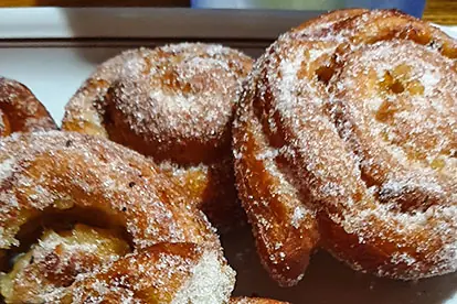 Zuckerbestreute Apfelschnecken auf einem Teller, goldbraun und frisch gebacken.