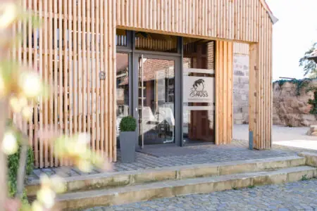 Eingang eines modernen Restaurants mit Holzverkleidung und stilvollem Logo, umgeben von einem einladenden Außenbereich.
