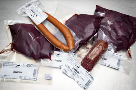 Verschiedene vakuumverpackte Fleischprodukte, darunter Wurst und Innereien, auf einer Arbeitsfläche.
