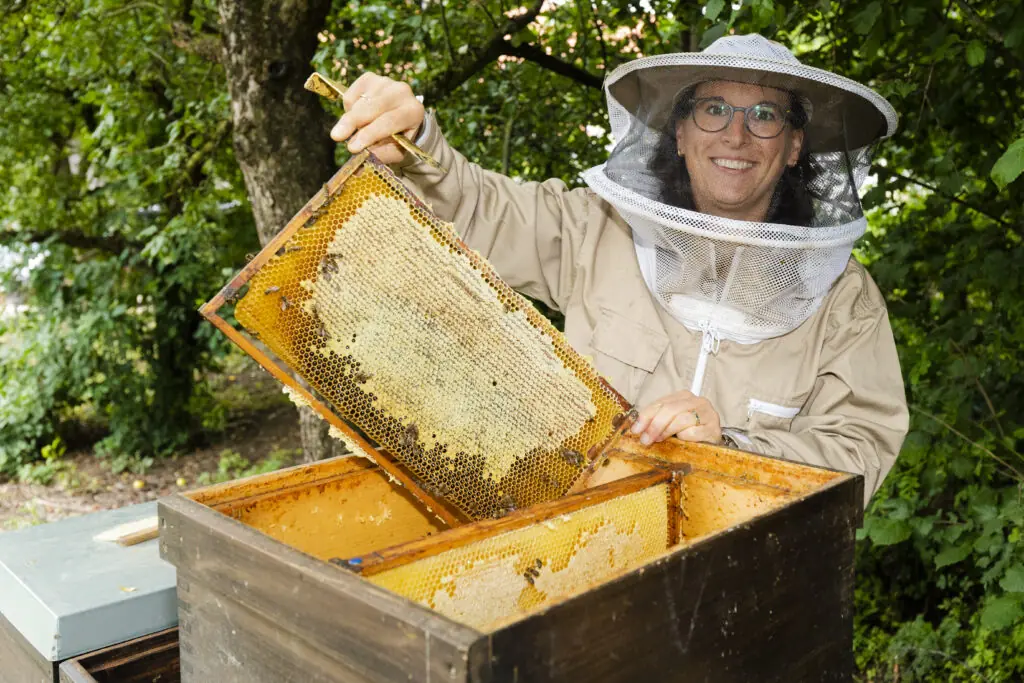 Eine Imkerin hält einen Wabenrahmen voller Honig in einem grünen Garten.