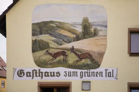 Wandmalerei eines Gasthauses mit Rehen und ländlicher Landschaft, betitelt "Gasthaus zum grünen Tal".