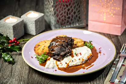 Herzhaftes Weihnachtsessen mit Rindfleisch, Kartoffelrösti und pürierten Kartoffeln, dekoriert mit festlicher Beleuchtung.