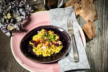 Festliches Gericht mit Quinoa, getrockneten Früchten und Nüssen auf einem eleganten Teller, umgeben von weihnachtlicher Dekoration.