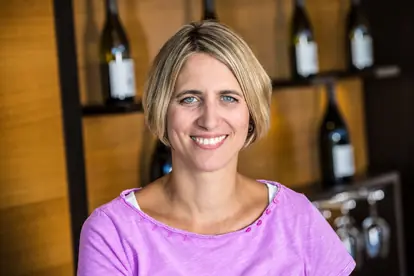 Lächelnde Frau in lila Shirt vor einer Weinregal, symbolisiert die Freude am alkoholfreien Glühwein.