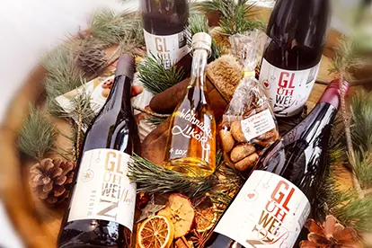 Bayerische Glühweine in festlicher Anordnung mit Gewürzen, Keksen und Dekoration auf einem rustikalen Untergrund.
