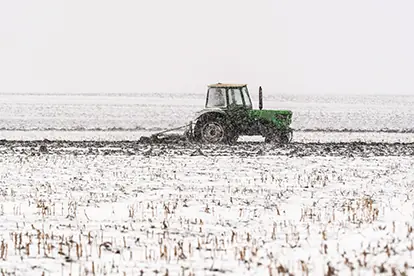 Ein Traktor pflügt ein verschneites Feld in winterlicher Landschaft.