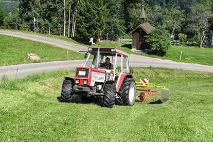 Traktor mäht Wiese neben dem Bergbauernhof Zeller, umgeben von grüner Landschaft und einem kleinen Holzgebäude.