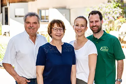Vier Personen lächeln in einer sonnigen Umgebung, repräsentieren ein freundliches Team oder eine Familie.