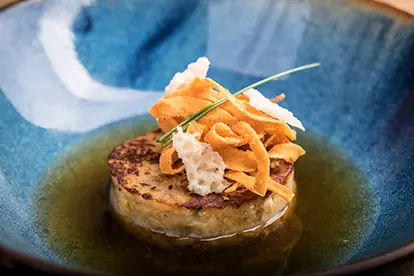 Kaspressknödel auf einer blauen Schale, garniert mit knusprigen Röstzwiebeln und frischem Schnittlauch in Brühe.