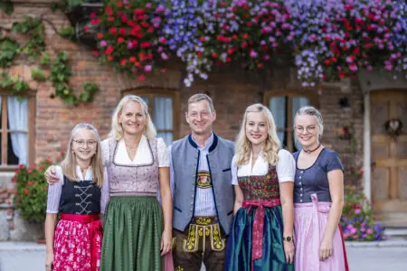 Fünf Personen in traditioneller bayerischer Tracht stehen vor einer blühenden Hausfassade.