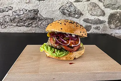 Bayerischer Burger mit Sesambrötchen, Salat, Tomate, Zwiebeln und einer speziellen Meerrettich-Preiselbeer-Sauce.