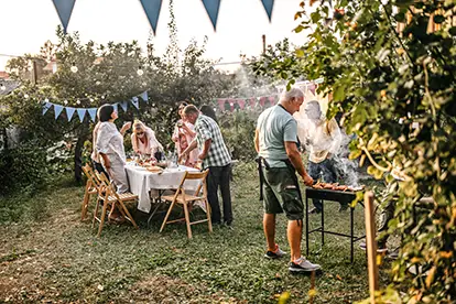 Eine gesellige Grillparty im Garten mit Freunden, umgeben von bunten Wimpeln und köstlichem Essen auf dem Grill.
