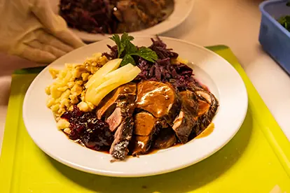 Ein Teller mit zartem Fleisch, Blaukraut, Spätzle und einer Sauce, garniert mit frischer Minze.