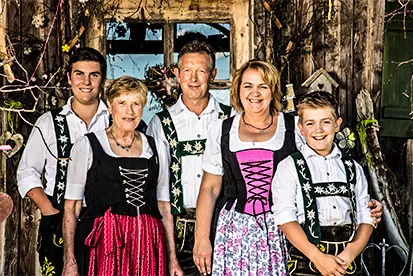 Familie in traditioneller Tracht vor einem Holzhaus, symbolisiert die Vielfalt und Tradition in der Heimat der Vielfalt.