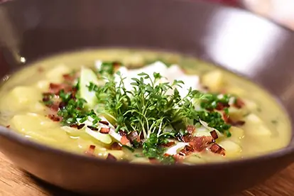 Kartoffel-Bier-Suppe in einer dunklen Schüssel, garniert mit Speck, Kräutern und einer cremigen Einlage.