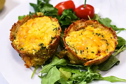 Kartoffelnester mit Cheddar, gefüllt mit Eiern und Kräutern, serviert auf Rucola und garniert mit Kirschtomaten.
