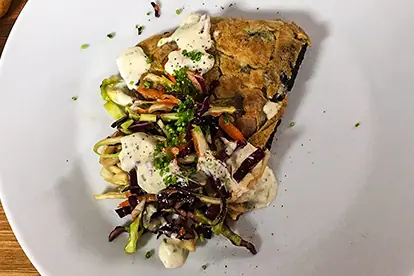 Kartoffel-Tortilla mit buntem Gemüse und einer cremigen Sauce auf einem weißen Teller angerichtet.
