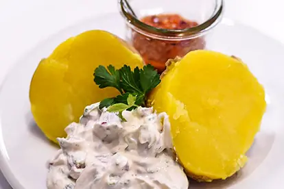 Pellkartoffeln mit cremigem Dip und einer Portion Chilisauce, garniert mit frischer Petersilie.