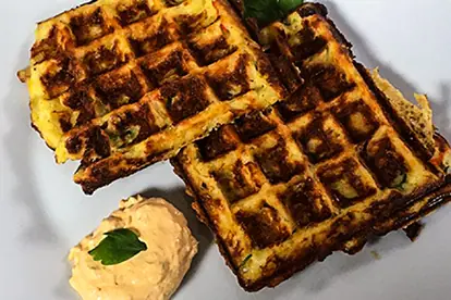 Herzhafte Kartoffel-Waffeln serviert mit einer cremigen Dip-Sauce und frischen Kräutern auf einem weißen Teller.