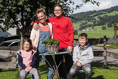 Familie posiert fröhlich im Freien mit einem Pflanztopf, ideal für die Hof Kuhn-Website.