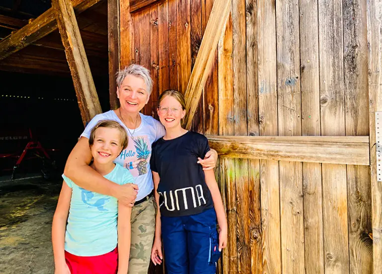 Familie posiert lächelnd vor einer Holzwand am Steinberger Hof.