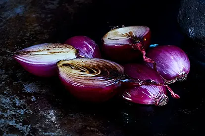 Geröstete rote Zwiebeln, die perfekt zu Blumenkohl geräuchert passen, auf einer dunklen Oberfläche platziert.