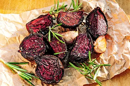 Gegrillte rote Bete auf Backpapier, garniert mit Rosmarin und Knoblauch, präsentiert eine köstliche Beilage.