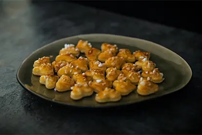 Zimt-Frischkäse-Hörnchen auf einem Teller, goldbraun gebacken und mit Zuckerstreuseln dekoriert.